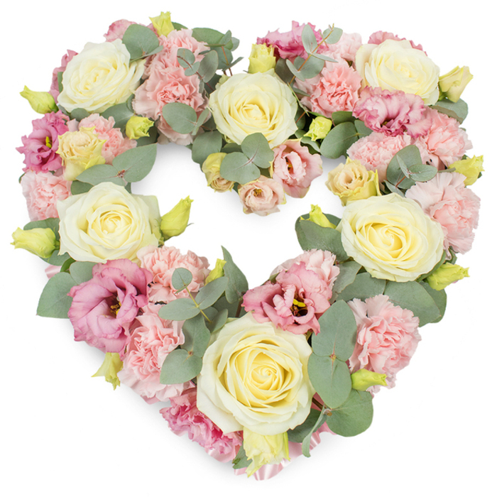 A generous heart-shaped funeral wreath, rich with pastel blooms and cool foliage, is shown against a bright white background that highlights its colours and contours. The heart is meticulously formed, with flowers placed so closely together that they create a smooth, continuous surface of petals. Cream and pale yellow roses are dotted across the wreath, their velvety, tightly layered centres opening into full, rounded blooms that draw the eye along the curve of the heart. Between these anchor blooms, light pink carnations cluster in soft groups, their frilly, multi-petalled heads adding a gentle, tactile quality that seems almost touchable. Among them, deeper shades of pink and mauve lisianthus introduce contrast; their somewhat looser, cup-shaped flowers, sometimes showing darker centres, lend a graceful, informal elegance. Threaded throughout, eucalyptus stems with round, silvery-green leaves offer a soothing counterpoint to the warm pastels, adding depth, shade, and a sense of airiness. Tiny yellow-green buds, some still tightly closed, nestle amongst the petals, hinting at vitality and the ongoing cycle of life. The overall mood of the piece is calm, loving, and reflective, a visual expression of comfort at times of loss. This kind of heart wreath would sit beautifully at a funeral service in Amersham, maybe in a quiet church near the River Misbourne or at a gathering in one of the town's chapels, where family and friends come together to remember. With the quiet craftsmanship you would expect from Flower Delivery Amersham, the tribute becomes a heartfelt symbol of sympathy, connection, and enduring affection.