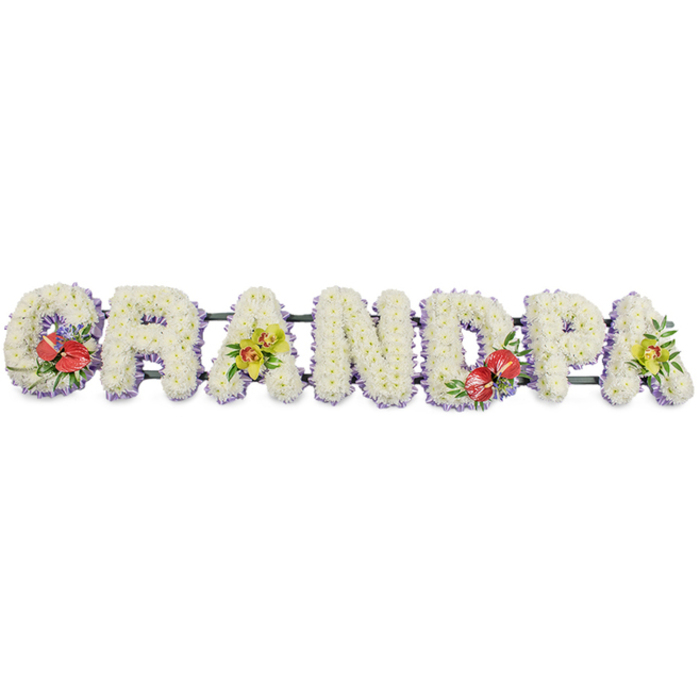 In this image, a striking line of floral lettering forms the word "GRANDPA," presented on a clean white background so that every detail is clearly visible. The tribute runs horizontally, each capital letter solid and weighty, yet softened by its covering of delicate white chrysanthemum blooms. The flowers are arranged tightly, petal against petal, to create a smooth, cushion-like surface that suggests comfort and peace. Their bright white colouring catches the light gently, producing a quiet glow that could easily sit at the heart of a funeral ceremony in Amersham, perhaps at a local church or crematorium near the town centre. Just beneath the flowers, a trim of pale lavender ribbon lines the base of each letter. This subtle band of colour outlines the shapes, adding a gentle pastel contrast and drawing the eye along the word from left to right. Strong, dark green bars run behind the letters, linking them together and providing the structural support needed for display by the coffin or at the graveside. To give the tribute warmth and individuality, the florist has incorporated standout accent sprays: deep red anthuriums with their glossy, heart-shaped faces and upright spadices adorn the "G" and the "D," nestled among lush green foliage and specks of tiny purple filler flowers. Meanwhile, the first and final "A" are decorated with clusters of yellow-green orchids, their elegant petals and buds stretching gracefully across the white chrysanthemums. This personalised GRANDPA floral arrangement feels both dignified and tender, the kind of design a family might order from Flower Delivery Amersham when they want to honour a grandfather's life with a meaningful, beautifully made tribute.